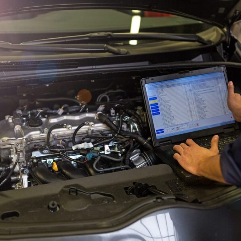 A mechanic using a laptop to diagnose an engine under the car's hood.