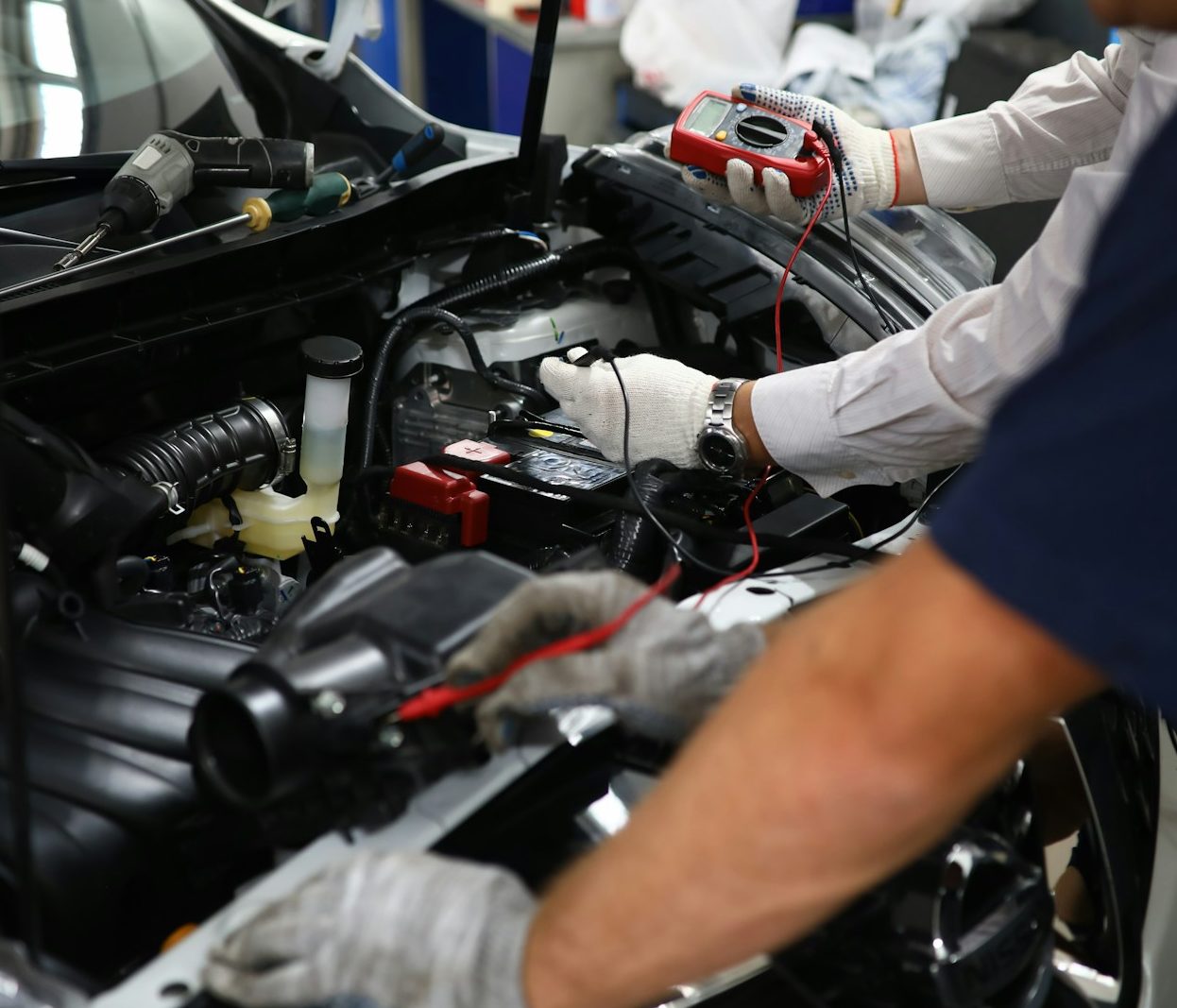 A technician using a multimeter on a car engine for diagnostic testing.