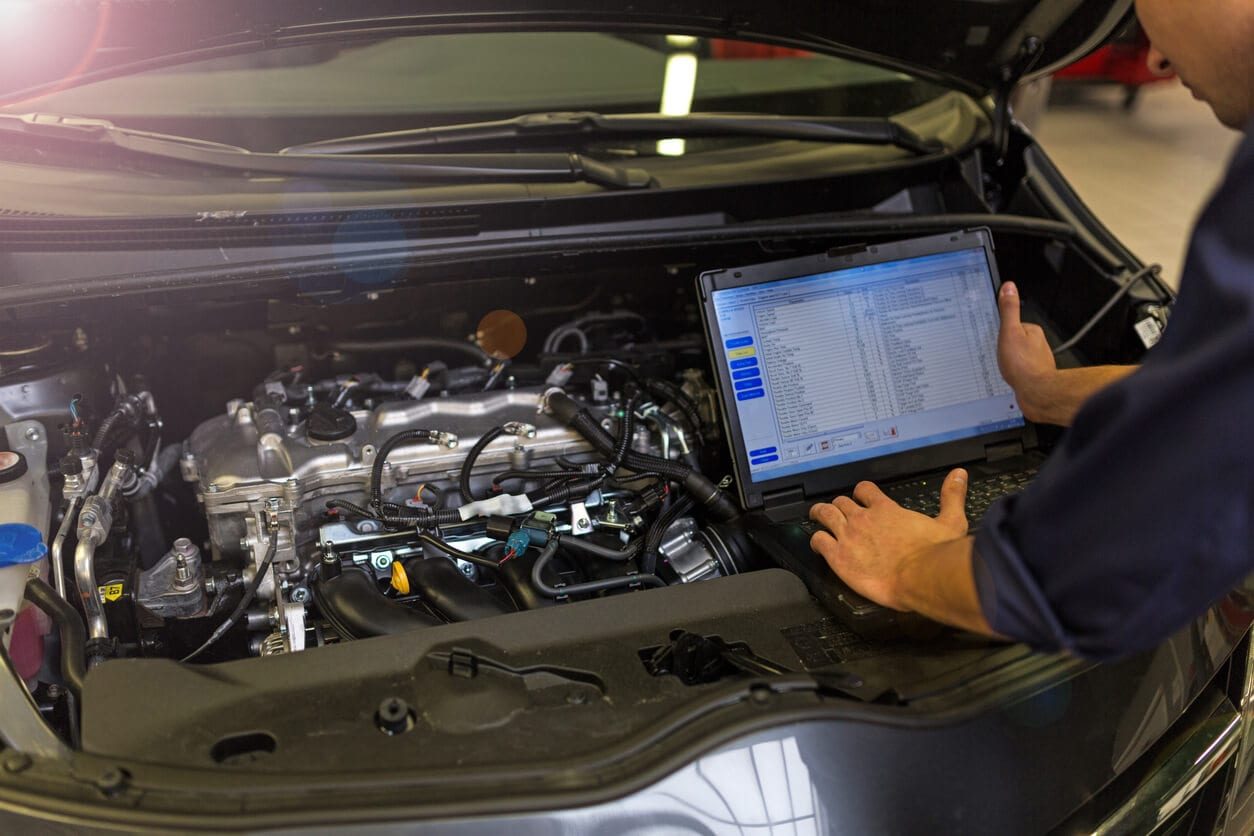 Mechanic using a laptop to diagnose an engine in a car.